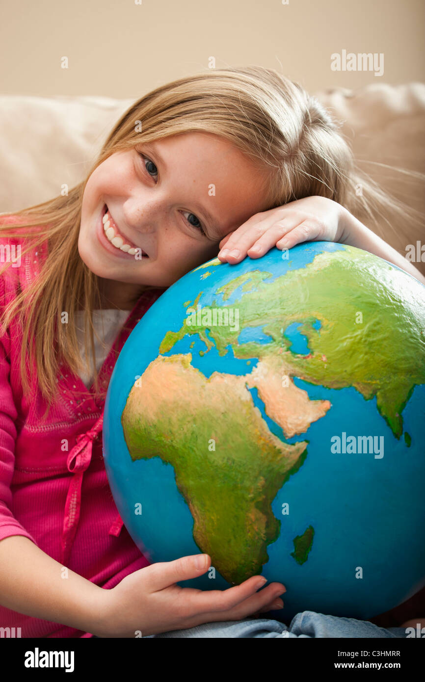 Cheerful girl (8-9) sitting on sofa with globe sur les genoux Banque D'Images