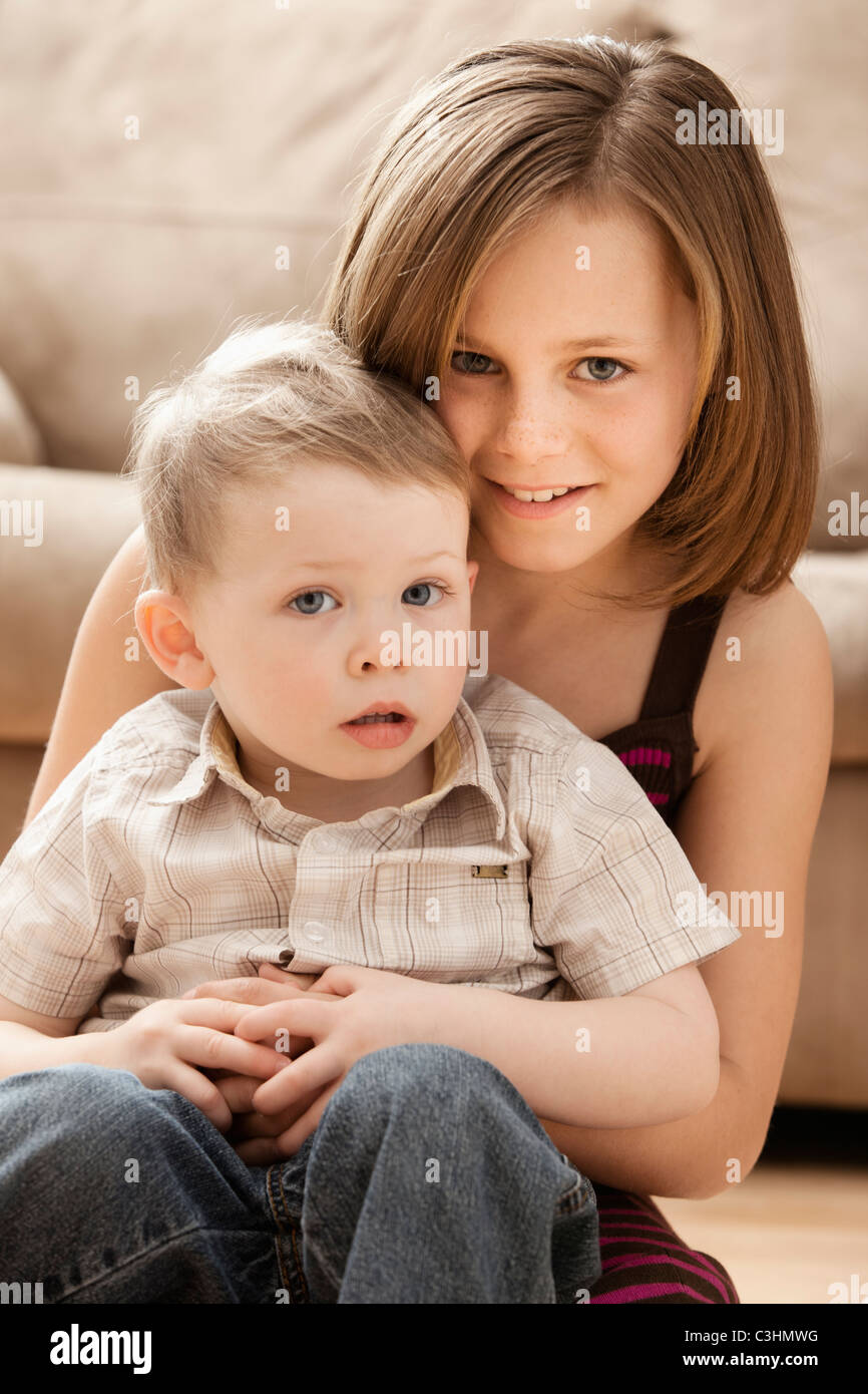 Portrait of Girl (10-11) avec le frère (2-3) sitting on floor Banque D'Images