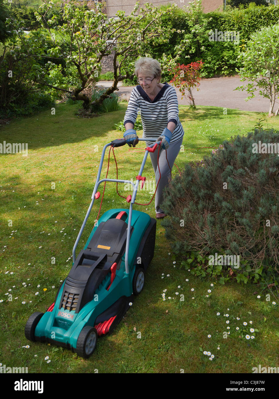 Femme plus âgée la pelouse avec une tondeuse électrique UK Banque D'Images
