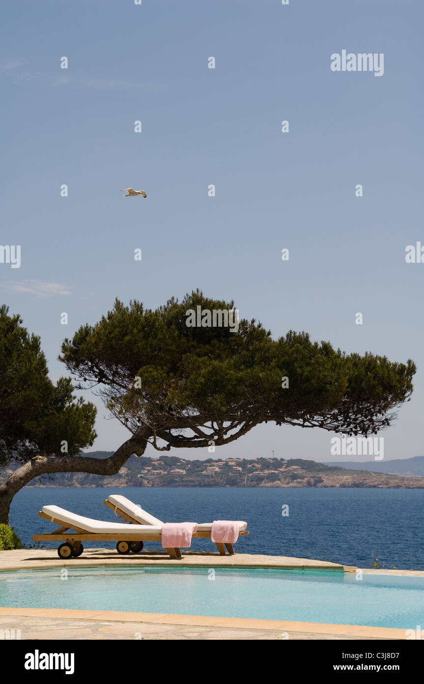 Des chaises longues sur le côté d'une piscine extérieure avec des cyprès et des vues sur la mer Méditerranée Banque D'Images