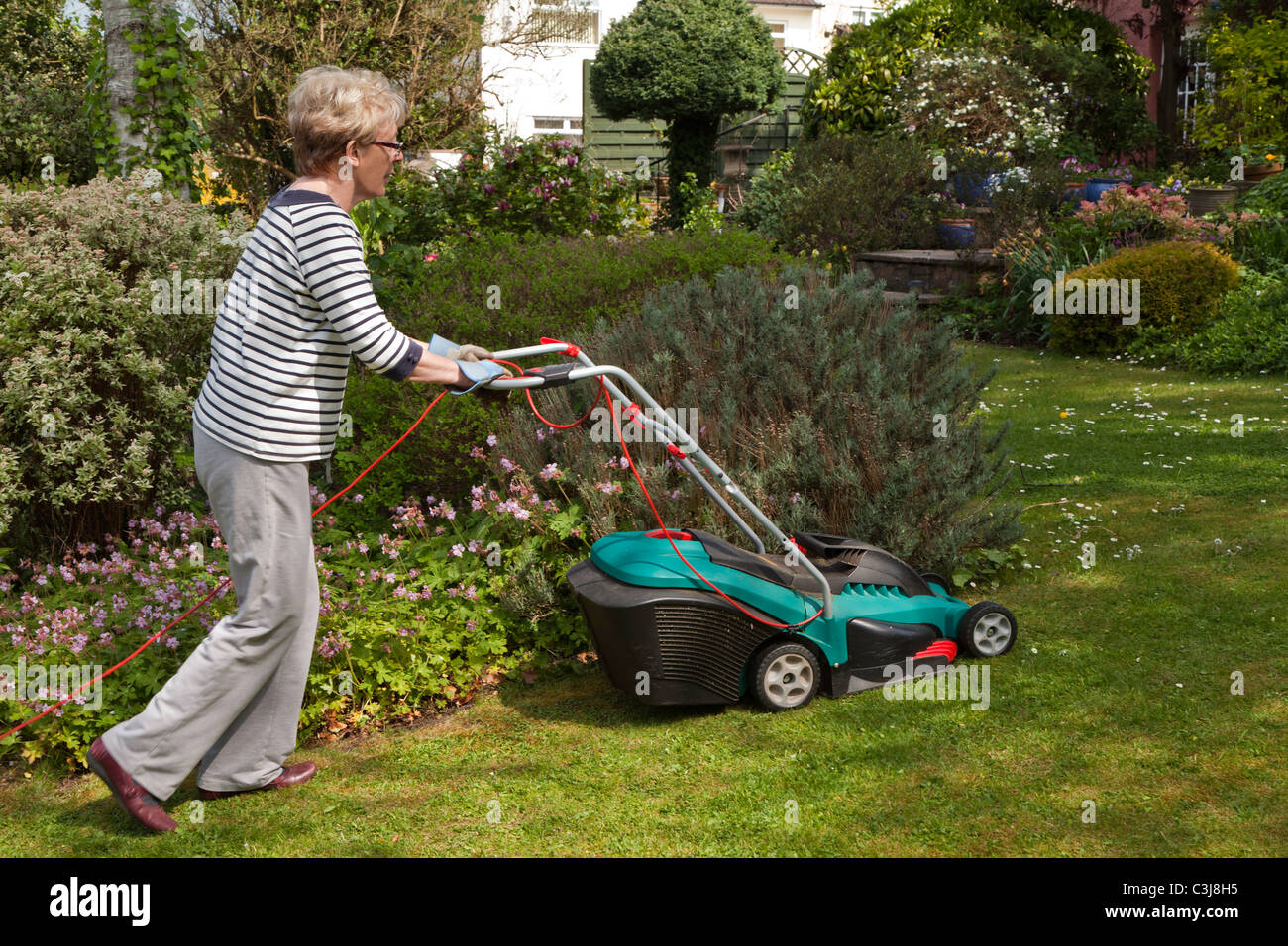 Femme plus âgée la pelouse avec une tondeuse électrique UK Banque D'Images