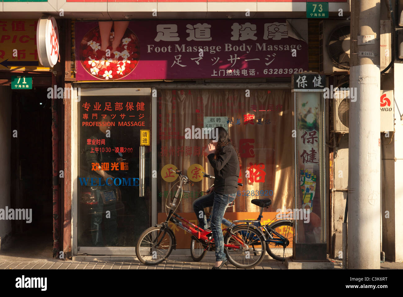 Femme sur un vélo se trouve à l'extérieur un salon de massage à Shanghai Chine Banque D'Images