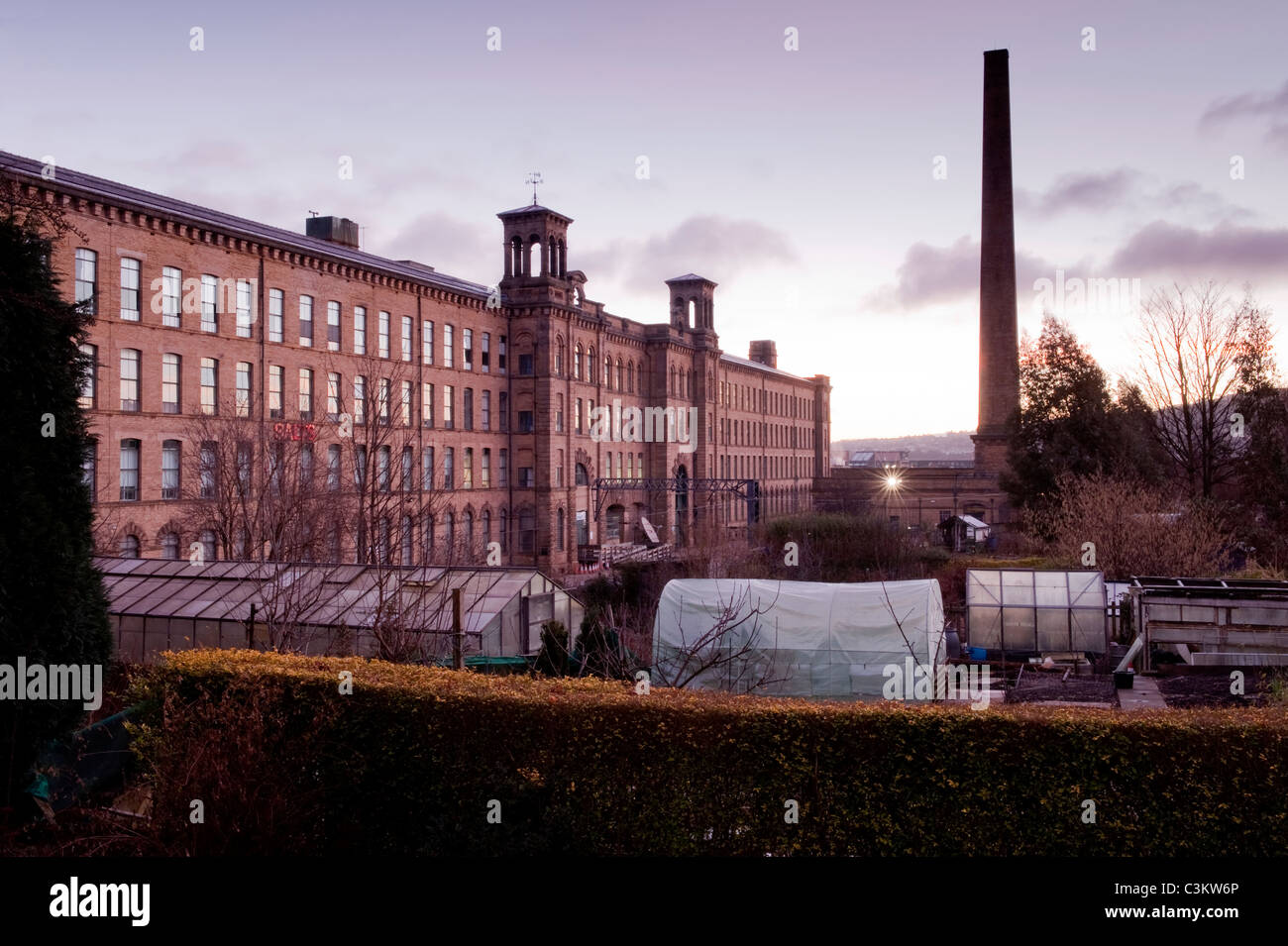 Salts Mill (cheminée et bâtiment historique de l'usine textile victorienne et serres dans les lotissements du village de Saltaire) au lever du soleil - Yorkshire, Angleterre, Royaume-Uni. Banque D'Images