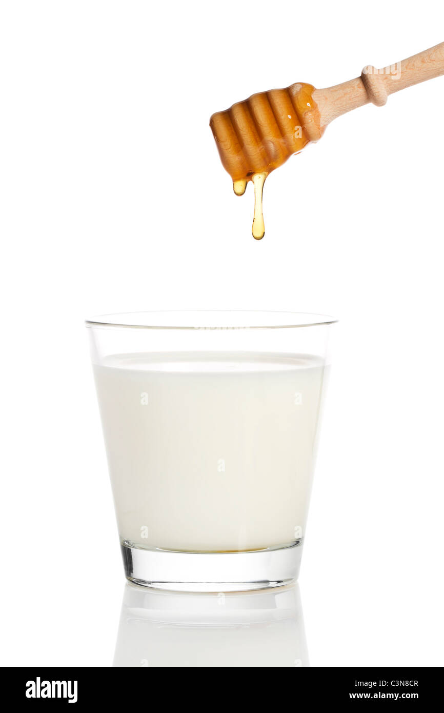 Gouttes de miel d'un balancier de miel dans un verre de lait sur fond blanc Banque D'Images