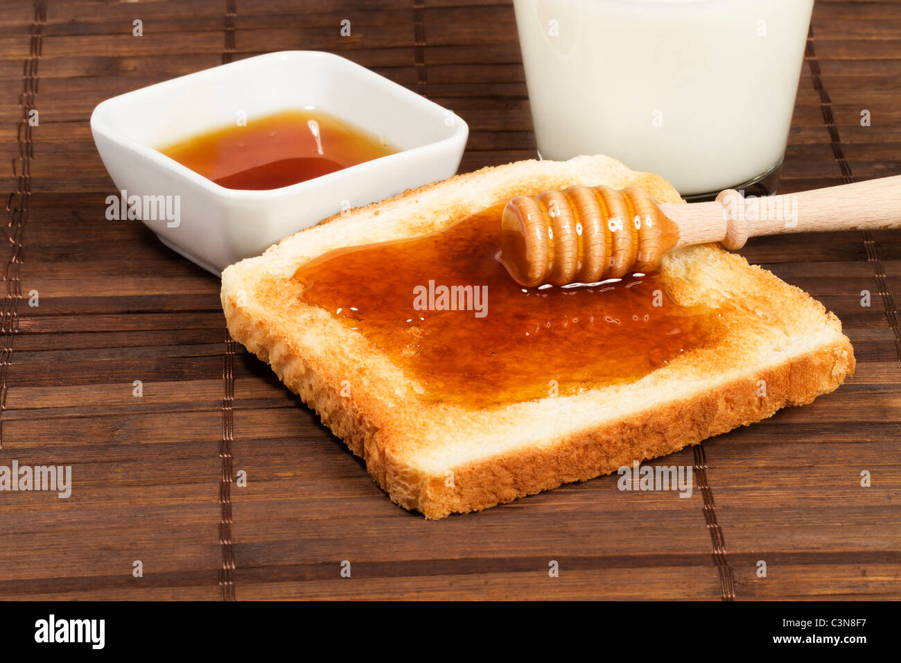 Le miel Le miel avec balancier sur un toast avec un verre de lait et un pot de miel Banque D'Images