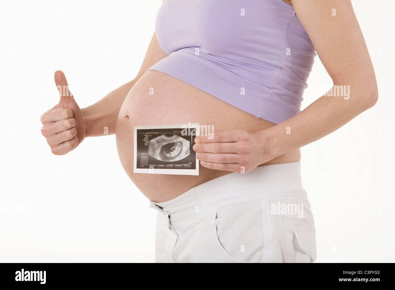 Pregnant woman holding sonogram image, showing Thumbs up sign, mid section Banque D'Images
