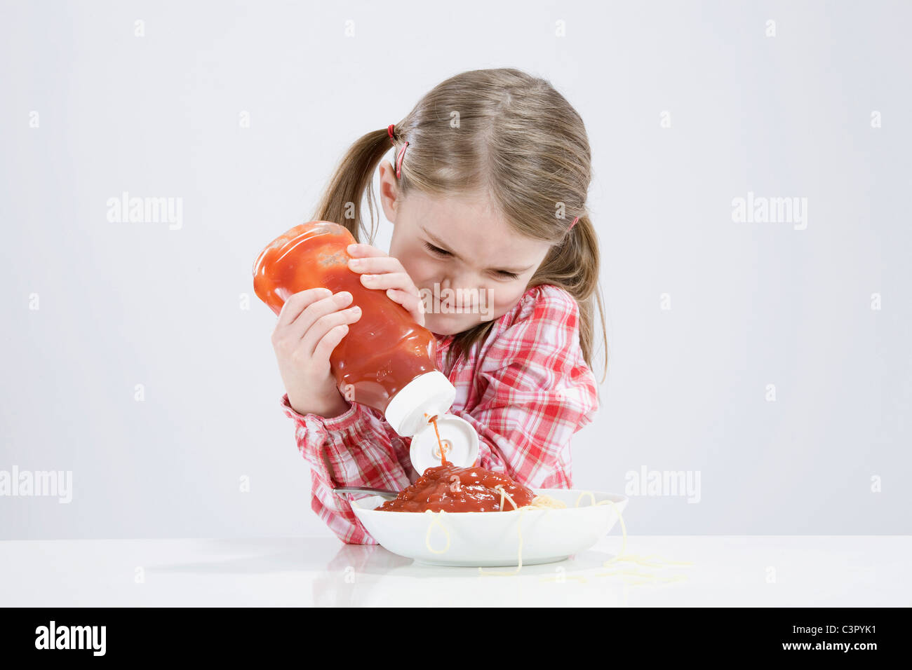 Girl (4-5) pouring ketchup sur spaghetti Banque D'Images