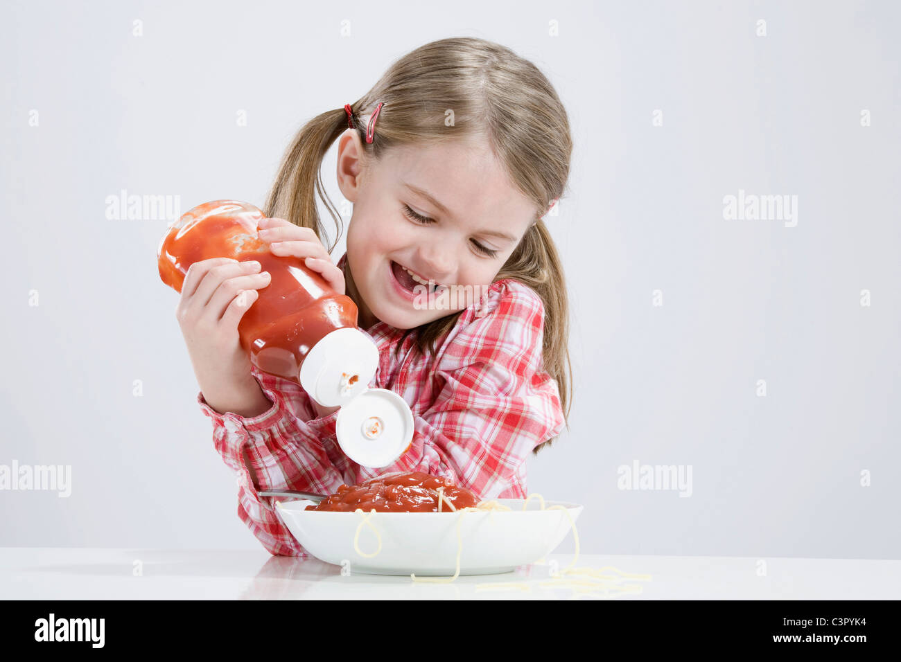 Girl (4-5) pouring ketchup sur spaghetti Banque D'Images