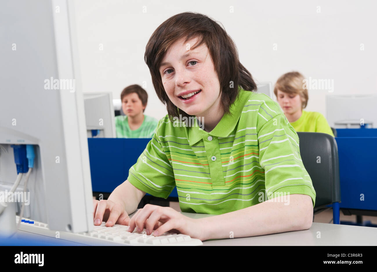 Allemagne, Emmering, Boy (12-13) smiling et à l'aide d'ordinateur avec les élèves en arrière-plan Banque D'Images