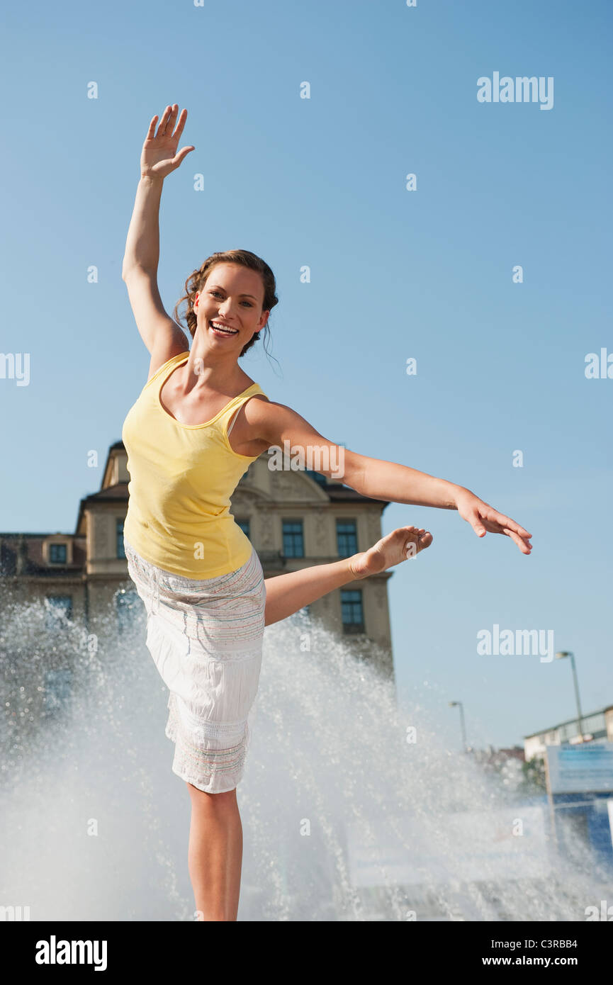 Allemagne, Munich, Karlsplatz, young woman standing on rock at Fountain Banque D'Images