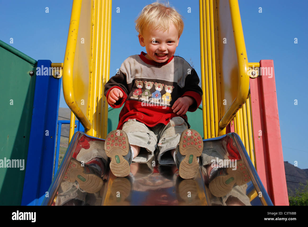 Un jeune garçon en haut d'une diapositive dans un parc de jeux pour enfants. Banque D'Images