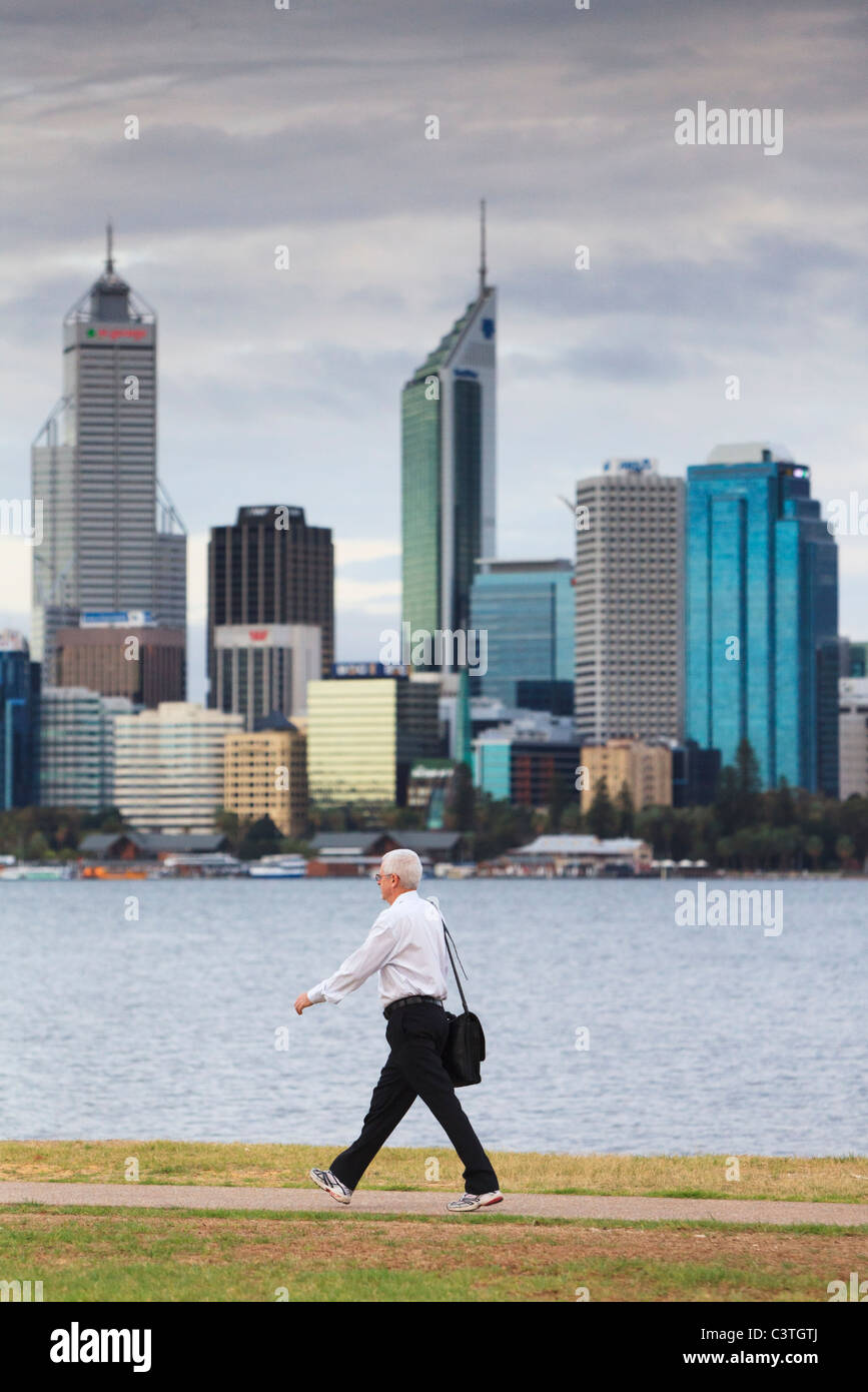 Homme portant un sac et porter un pantalon, une chemise et des chaussures de course sur sa façon de travailler avec les gratte-ciel dans la distance. Banque D'Images