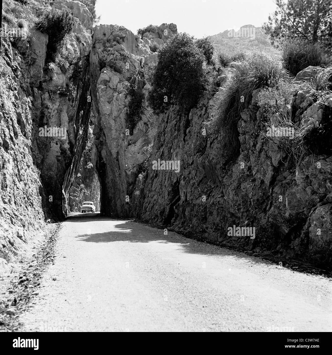 Années 1950. Dans ce tableau historique, nous voyons une voiture passe sous un tunnel naturel fabriqué à partir de roche dans la campagne espagnole. Banque D'Images