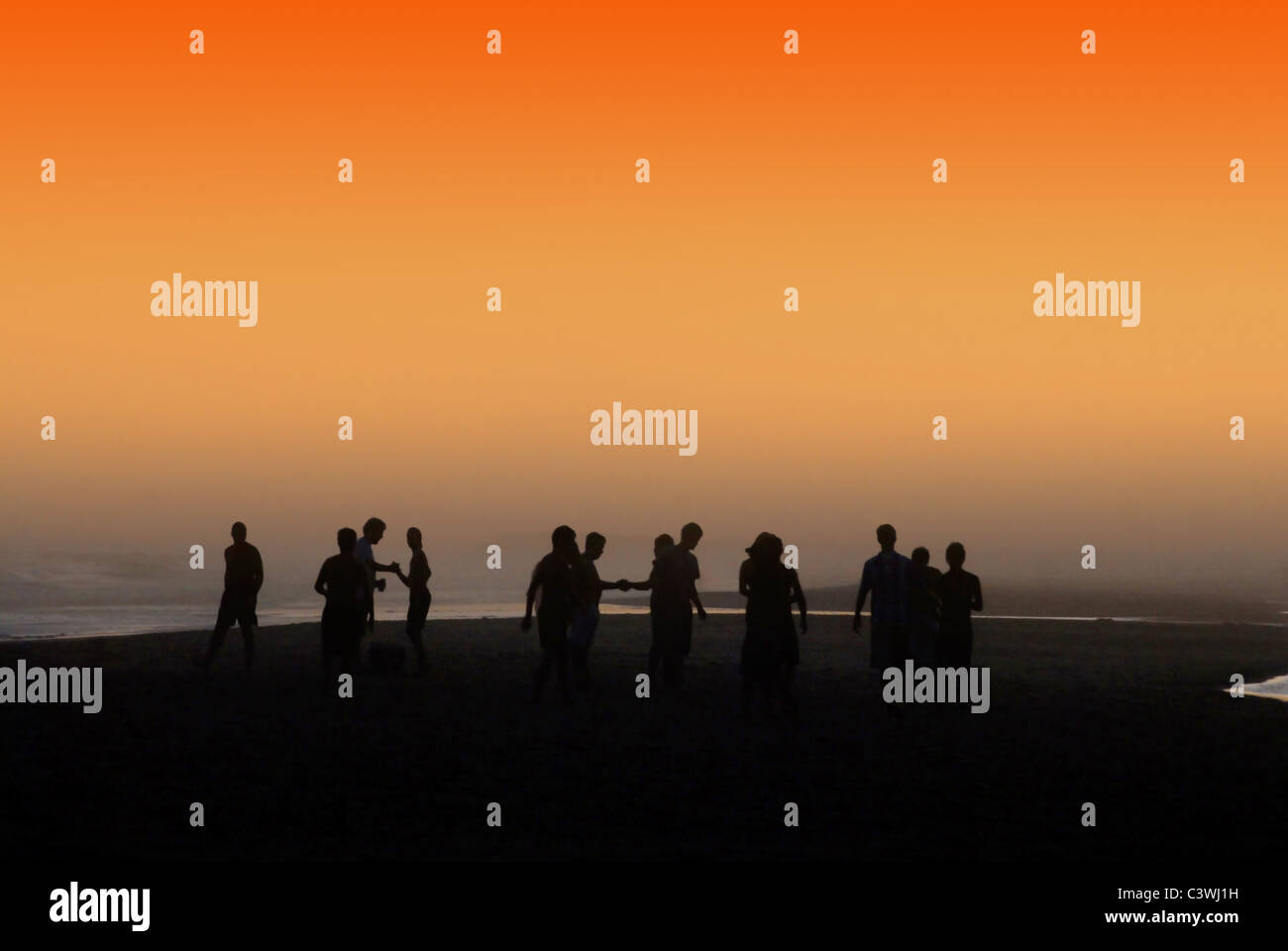 La silhouette du people socializing at la plage orange sous le coucher du soleil. Banque D'Images