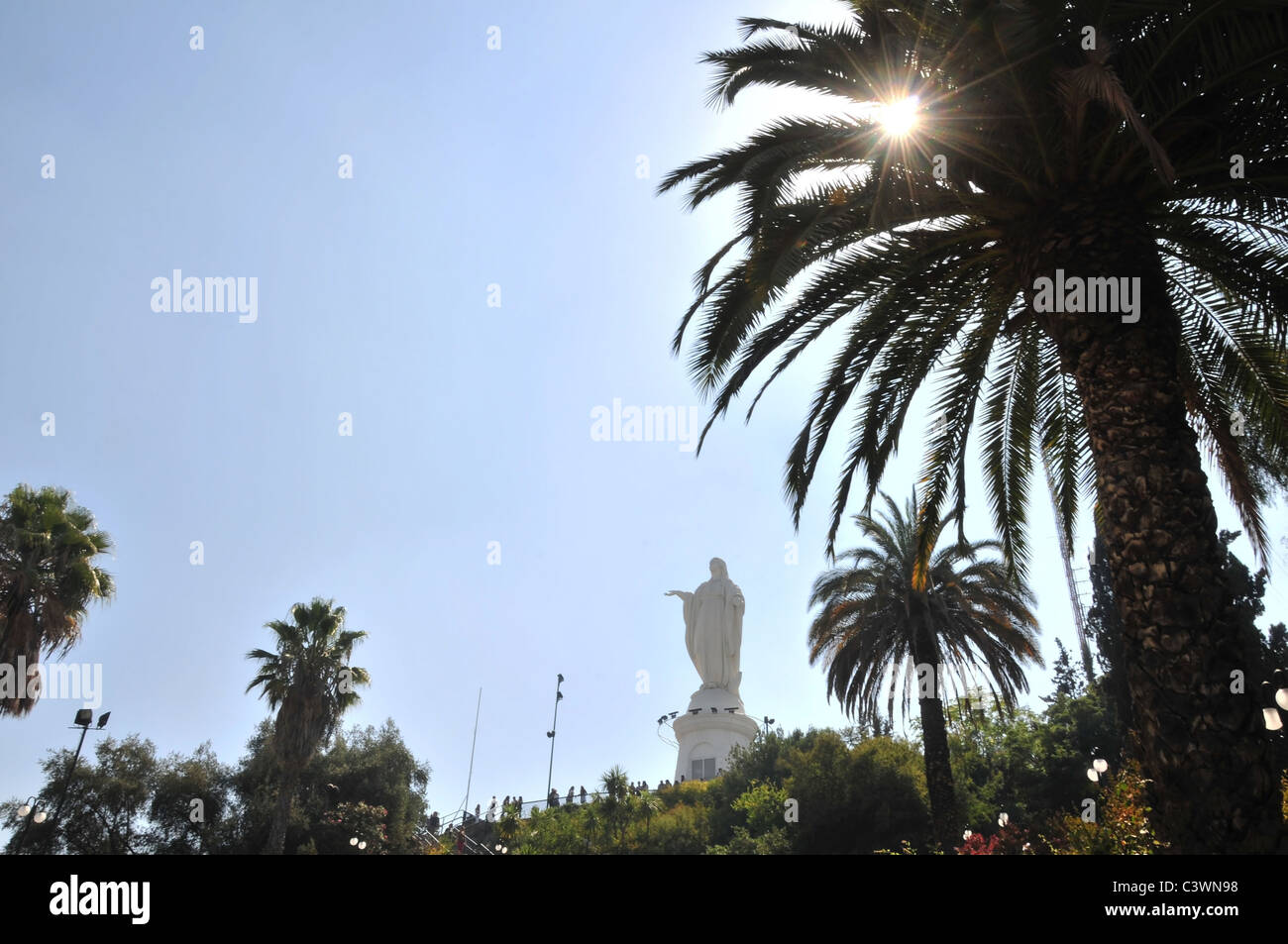 Statue de la Vierge Marie, avec le soleil qui brillait à travers un avant-plan palmier, sommet, colline de San Cristobal, Santiago, Chili Banque D'Images