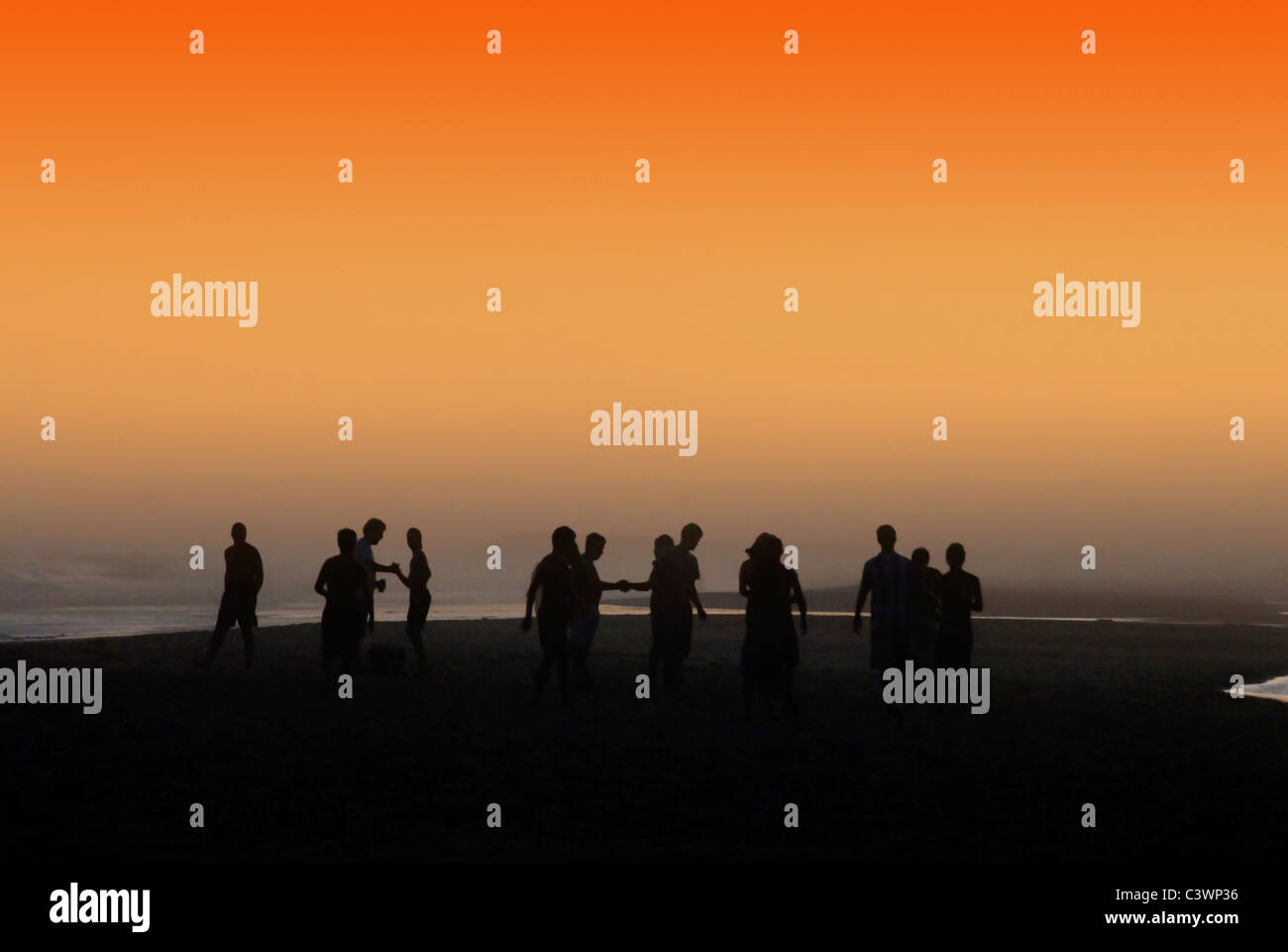 La silhouette du people socializing at la plage orange sous le coucher du soleil. Banque D'Images