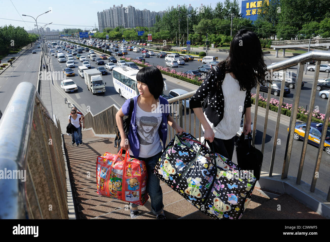 Filles migrants chinois hauling assurance aller sur une passerelle au-dessus de l'énorme flux de trafic à Beijing, Chine. 22-mai-2011 Banque D'Images