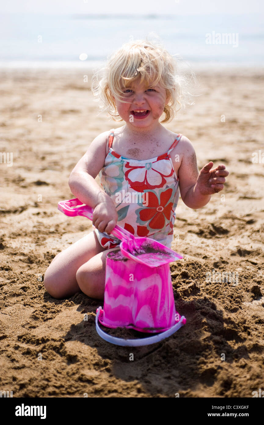 Portrait vertical d'une petite fille sur la plage à faire des châteaux sur une journée ensoleillée. Banque D'Images