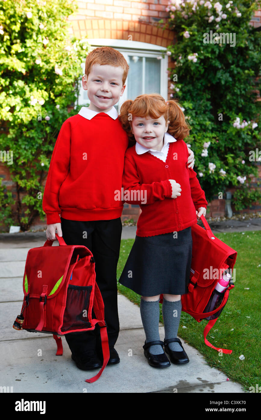 Une fillette de 4 ans avec du gingembre cheveux sur sa première journée d'école, avec son frère de 6 ans. Tant dans l'uniforme scolaire. Banque D'Images