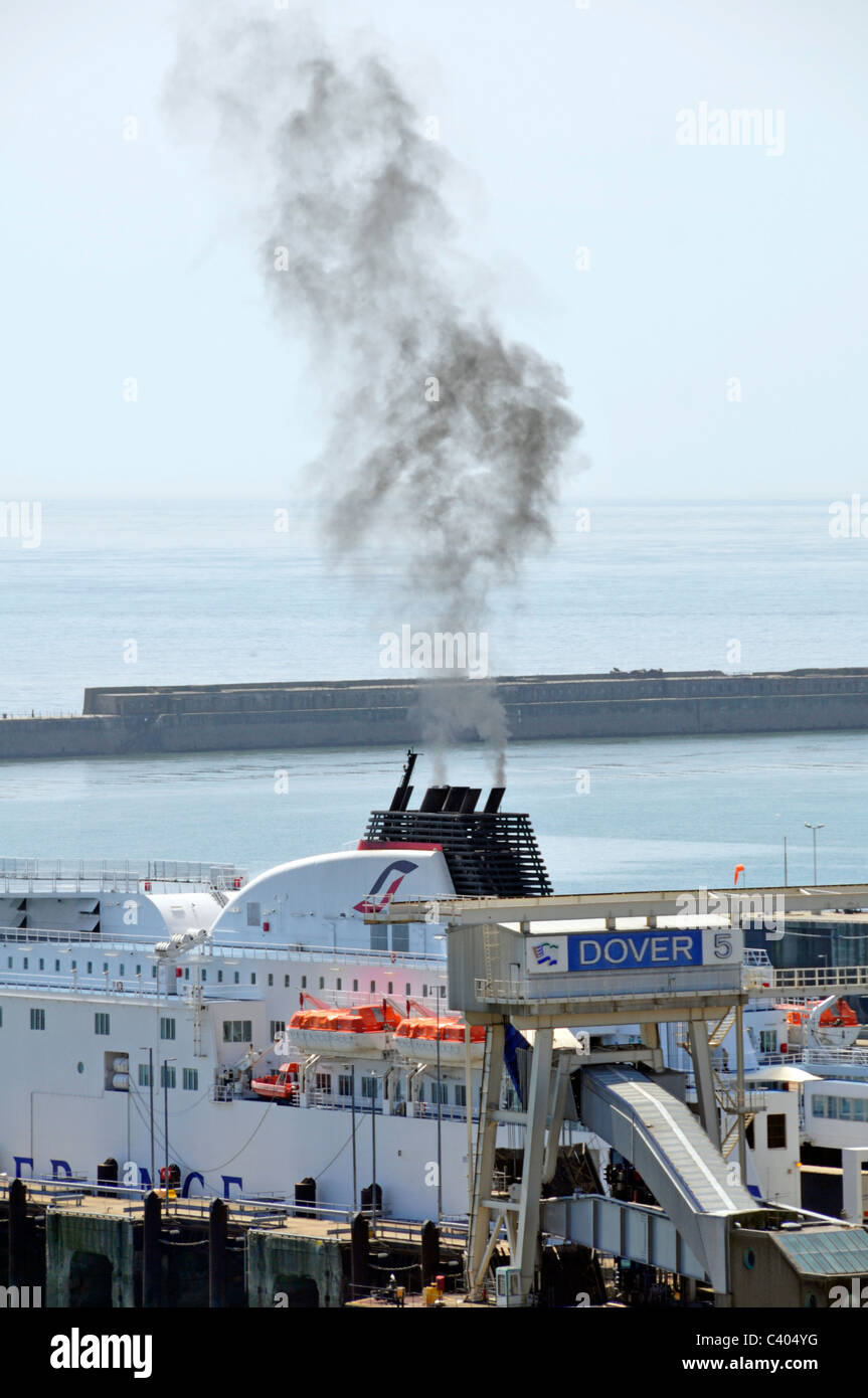 La fumée noire s'élevant dans l'atmosphère de funnel d'attente à partir de navires transbordeurs mur du port au-delà de Douvres ferry port Kent England UK Banque D'Images