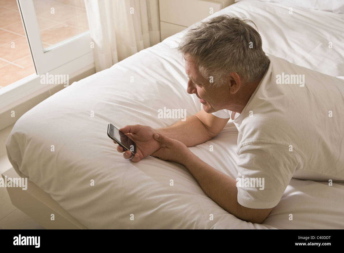 Homme mature sur lit à l'aide de smart phone Banque D'Images