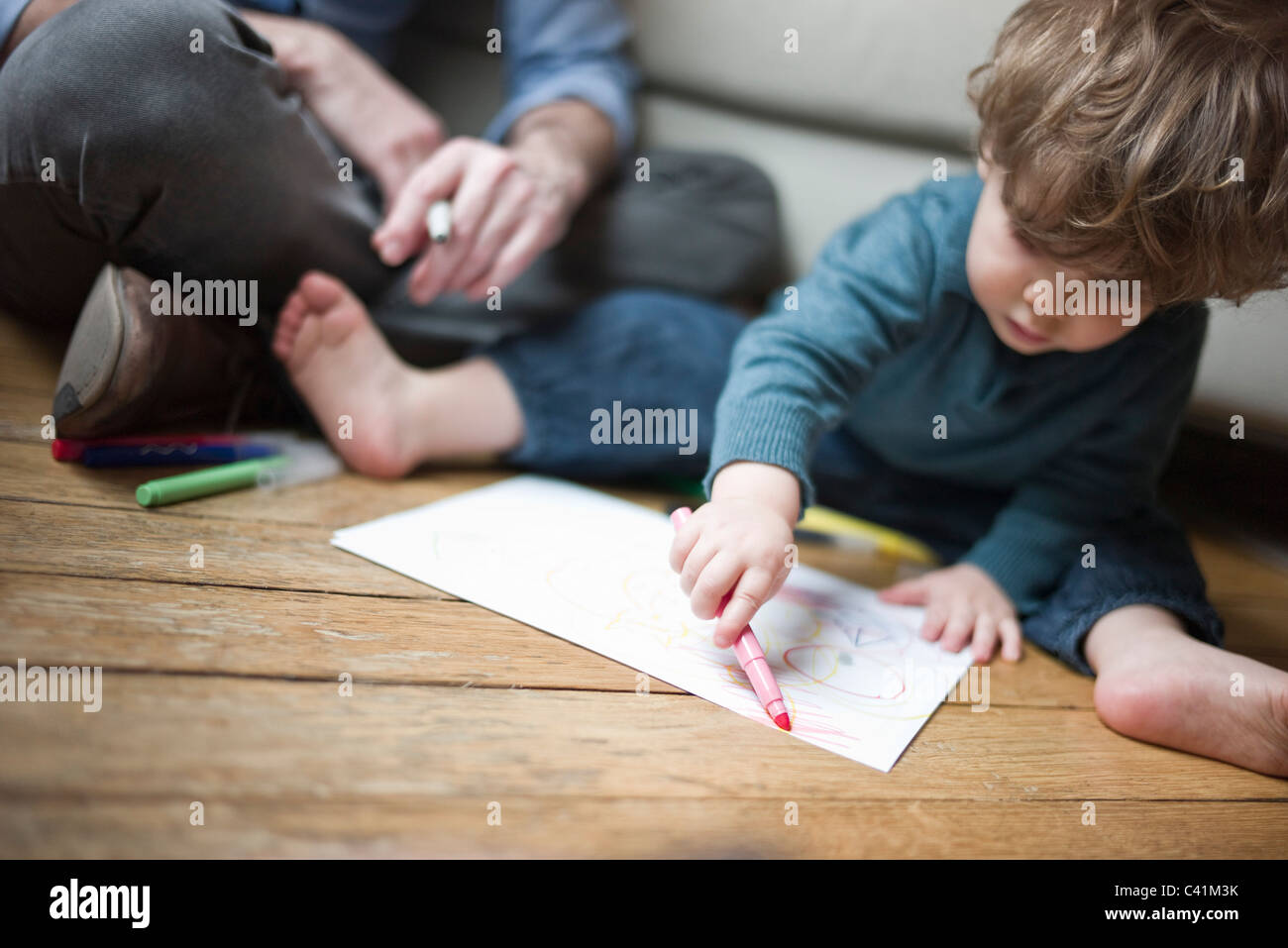 Tout-petit garçon assis sur le plancher avec un parent, dessin sur papier Banque D'Images