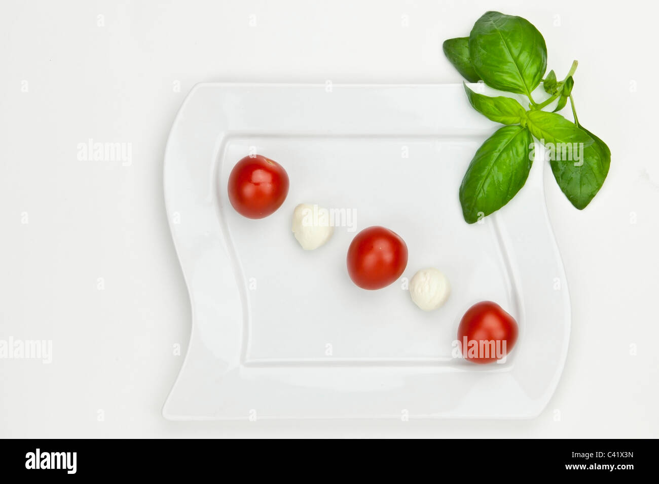 Boules de mozzarella avec tomates cerises sur une plaque blanche Banque D'Images