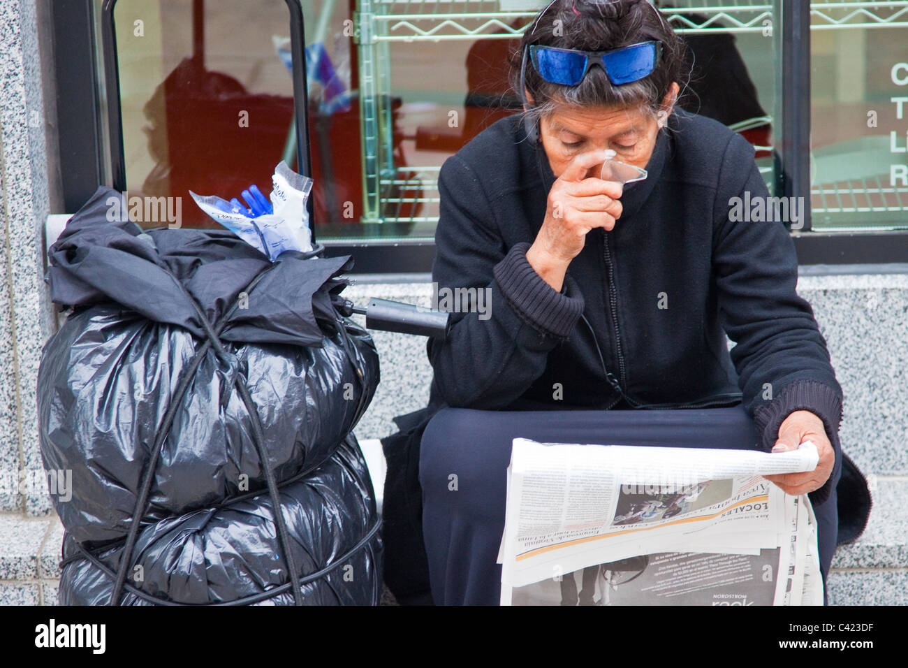 Femme sans-abri à l'aide d'un bas d'une bouteille cassée pour lire le journal, Washington DC Banque D'Images