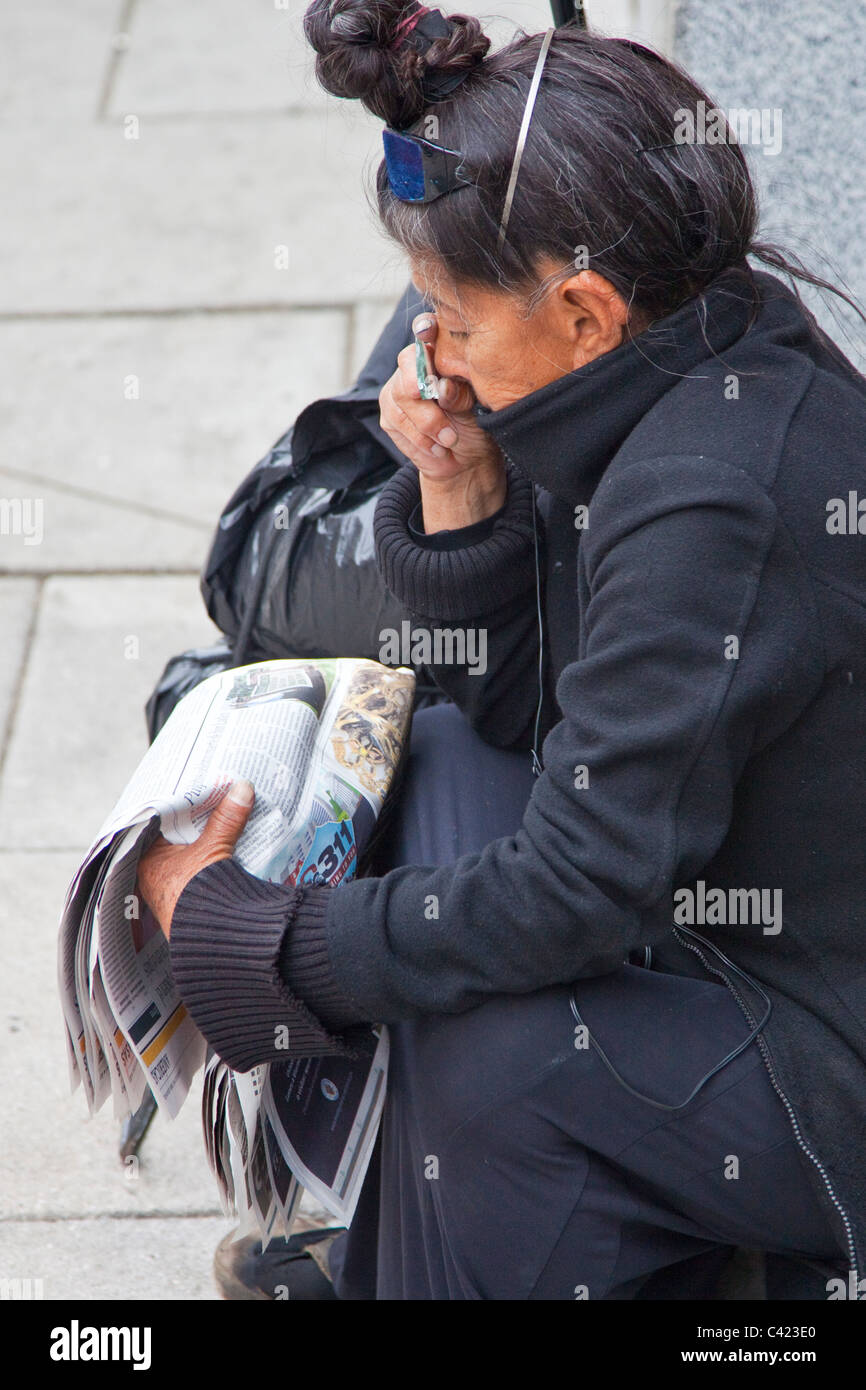 Femme sans-abri à l'aide d'un bas d'une bouteille cassée pour lire le journal, Washington DC Banque D'Images