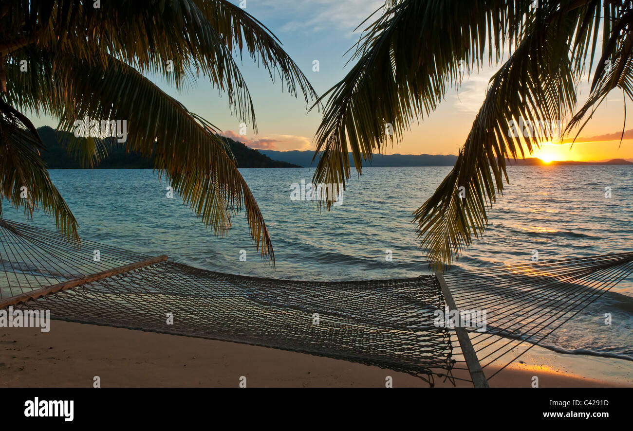 Hamac et de palmiers sur la plage au coucher du soleil, Matangi Private Island Resort, Îles Fidji. Banque D'Images