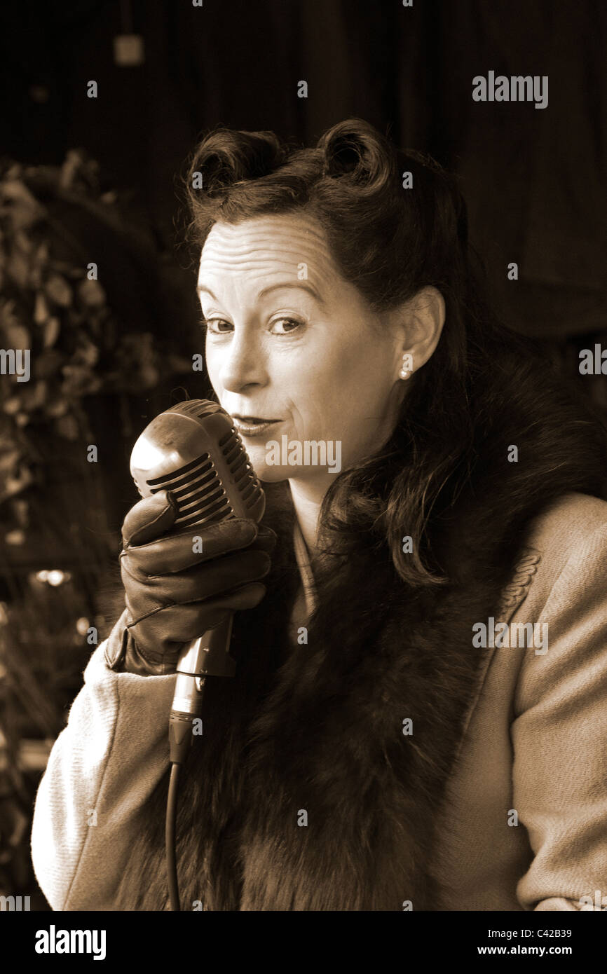 Deuxième Guerre mondiale des années 1940. Deuxième Guerre mondiale; réacteur Katie Spitfire oortrait d'une chanteuse qui tient un vieux microphone de diffusion, un artiste de la guerre dans une reconstitution à une gare ferroviaire britannique. Le week-end de la guerre des 40 acteurs, mode et coiffure à la station de Rawtenstall, Lancashire, mai 2011 Banque D'Images