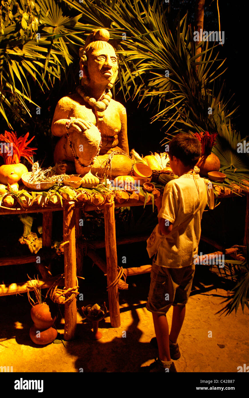 Mexican boy looking at Ssatue d'une fertilité Ixchel, déesse maya et de la lune, entouré d'offrandes, Xcaret park, Riviera Maya, Quintana Roo, Mexique Banque D'Images