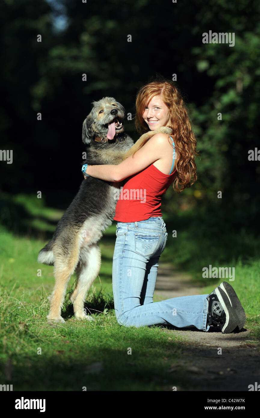Mongrel (Canis lupus familiaris). Jeune fille à genoux sur un chemin en bois tout en embrassant son chien. L'Allemagne. Banque D'Images