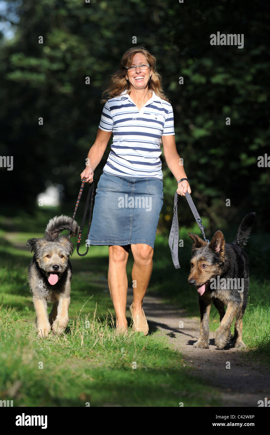 Mongrel (Canis lupus familiaris). Femme marchait sur un chemin de bois avec deux chiens en laisse. L'Allemagne. Banque D'Images
