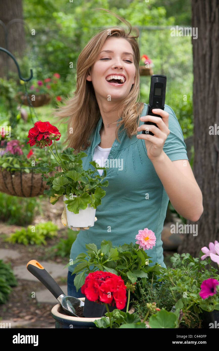 Jolie jeune femme planter des fleurs dans son jardin pendant que on cell phone Banque D'Images