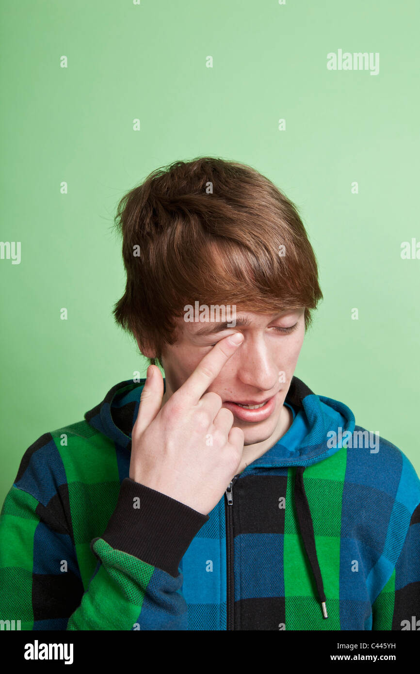 Un adolescent se frotter l'œil avec son doigt, portrait, studio shot Banque D'Images
