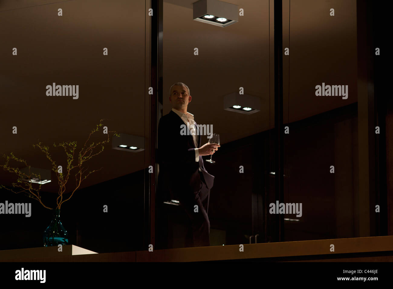 L'homme bien habillé avec un verre de vin à la fenêtre de l'appartement. Banque D'Images