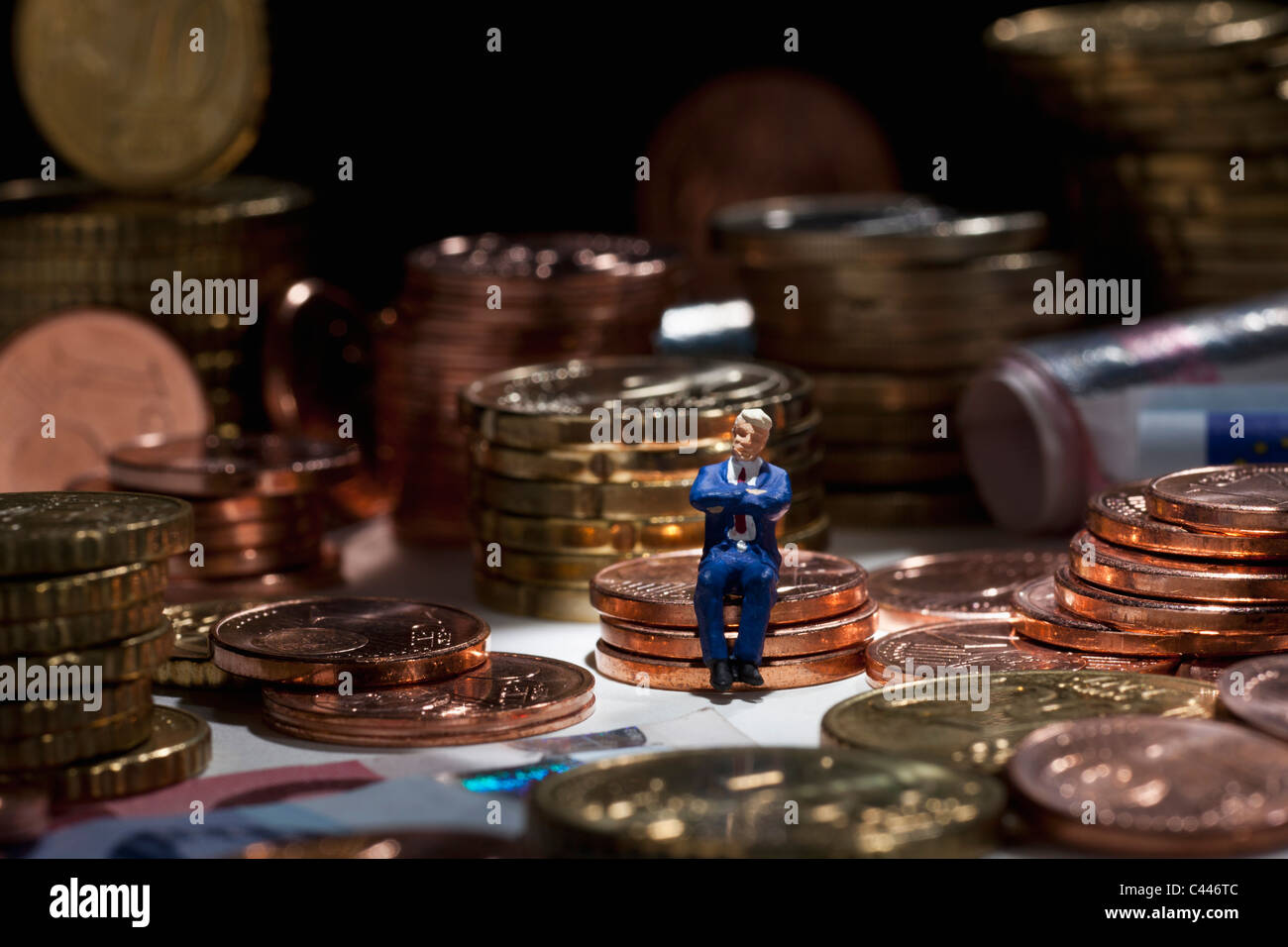 Un homme miniature, figurine avec les bras croisés assis sur une pile de pièces Banque D'Images