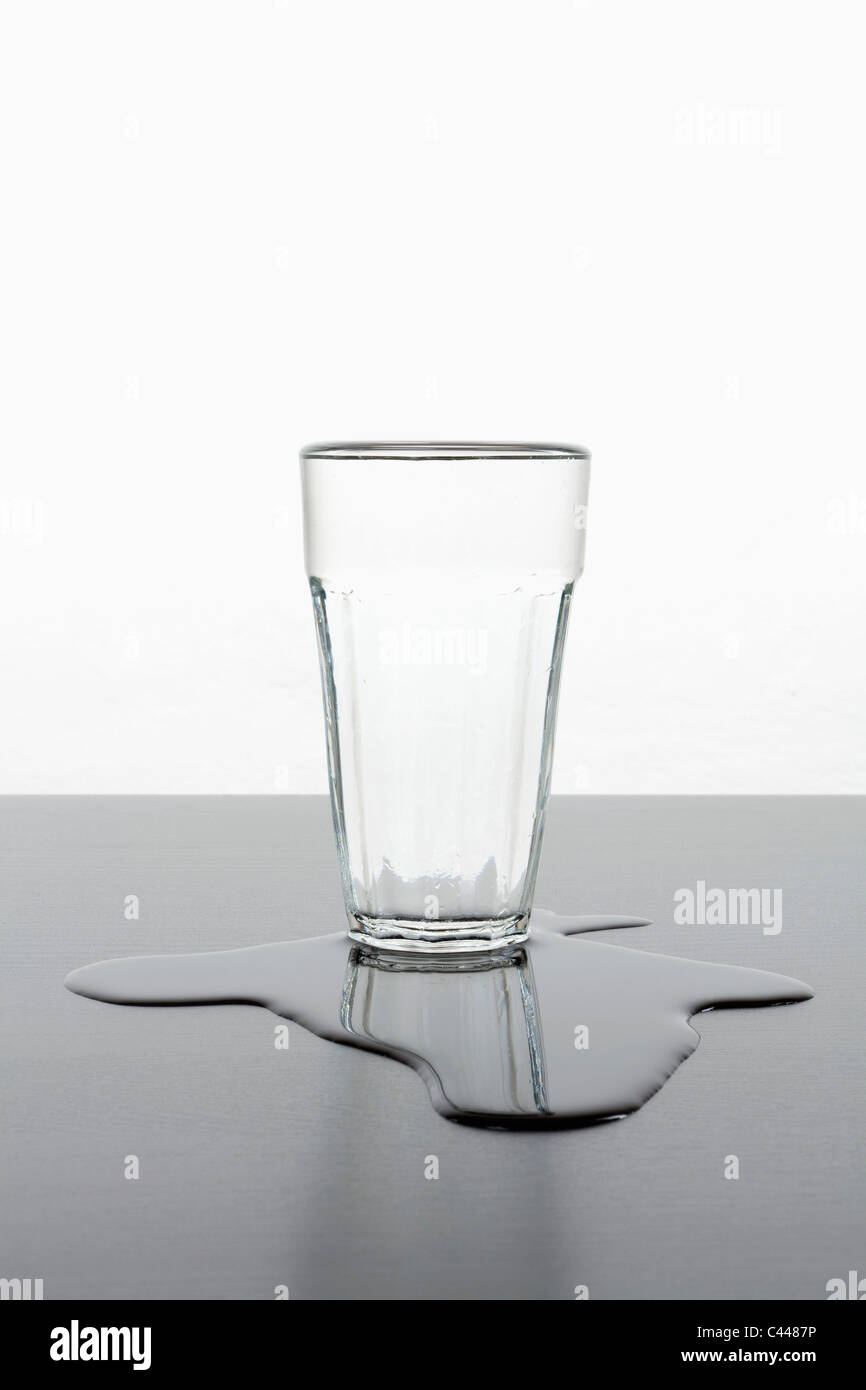 Un verre debout debout dans une flaque d'eau répandue Banque D'Images