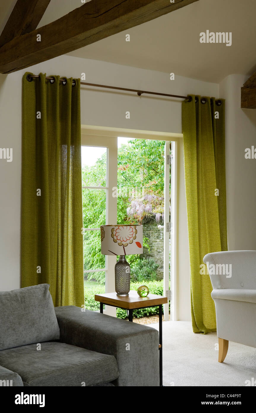 Grange transformée en salle de séjour avec poutres au plafond, rideaux verts et gris canapé Banque D'Images