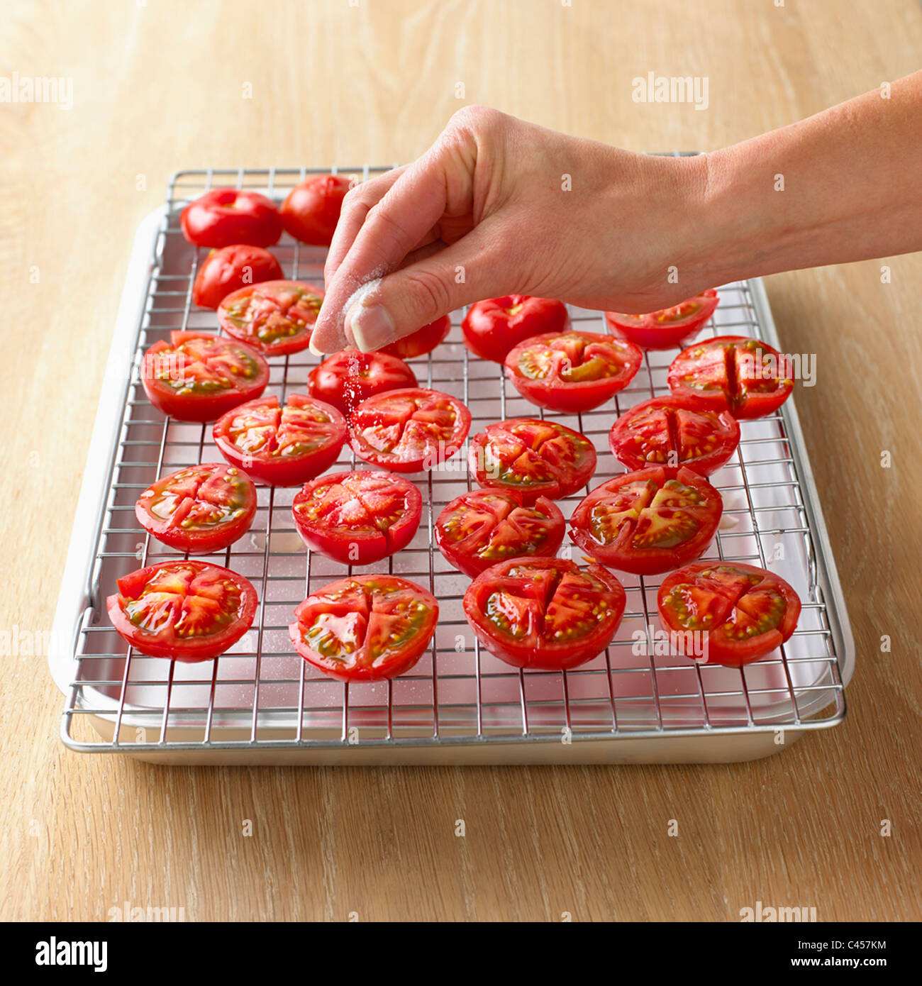 L'arrosage à la main du sel sur les moitiés de tomate, close-up Banque D'Images