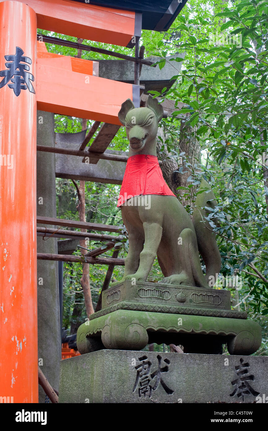 Red-bibbed fox statue et une partie de l'orange de torii à Fushimi-Inari Taisha, Kyoto, Japon. Banque D'Images