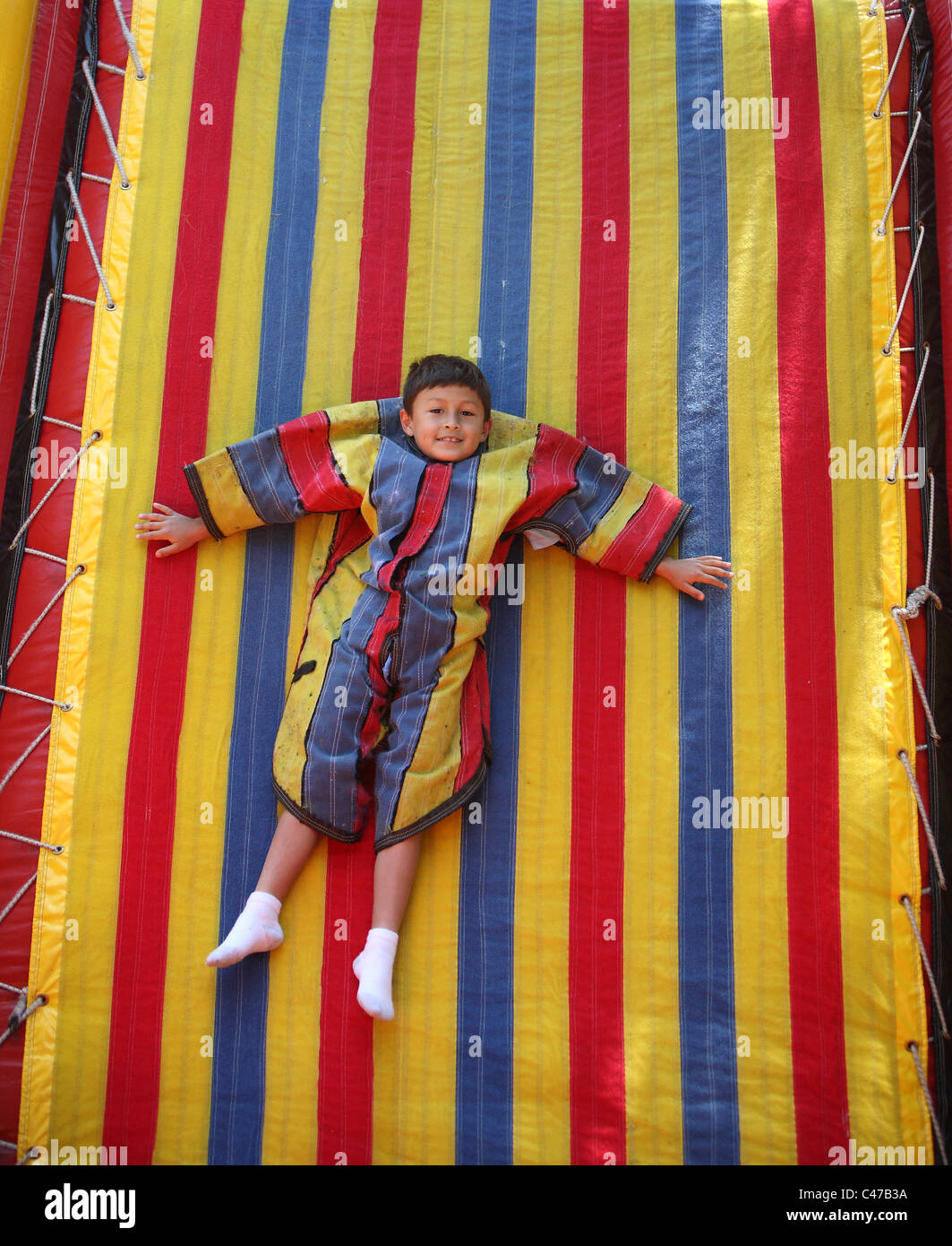 Garçon jouant sur le mur en velcro collant costume coloré Banque D'Images