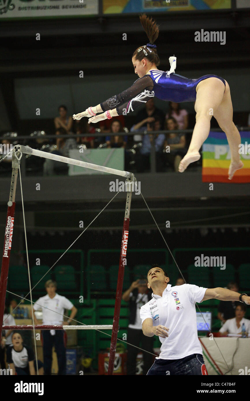 Compétition de gymnastique : Carlotta Ferlito effectuant un saut au barres asymétriques. L'entraîneur est prêt à la soutenir. Banque D'Images