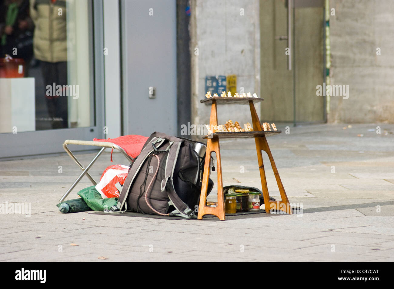 Configuration de rue avec un sac à dos, un tabouret pliant et un petit écran d'échecs disposés sur un trottoir dans une zone commerciale urbaine. Banque D'Images