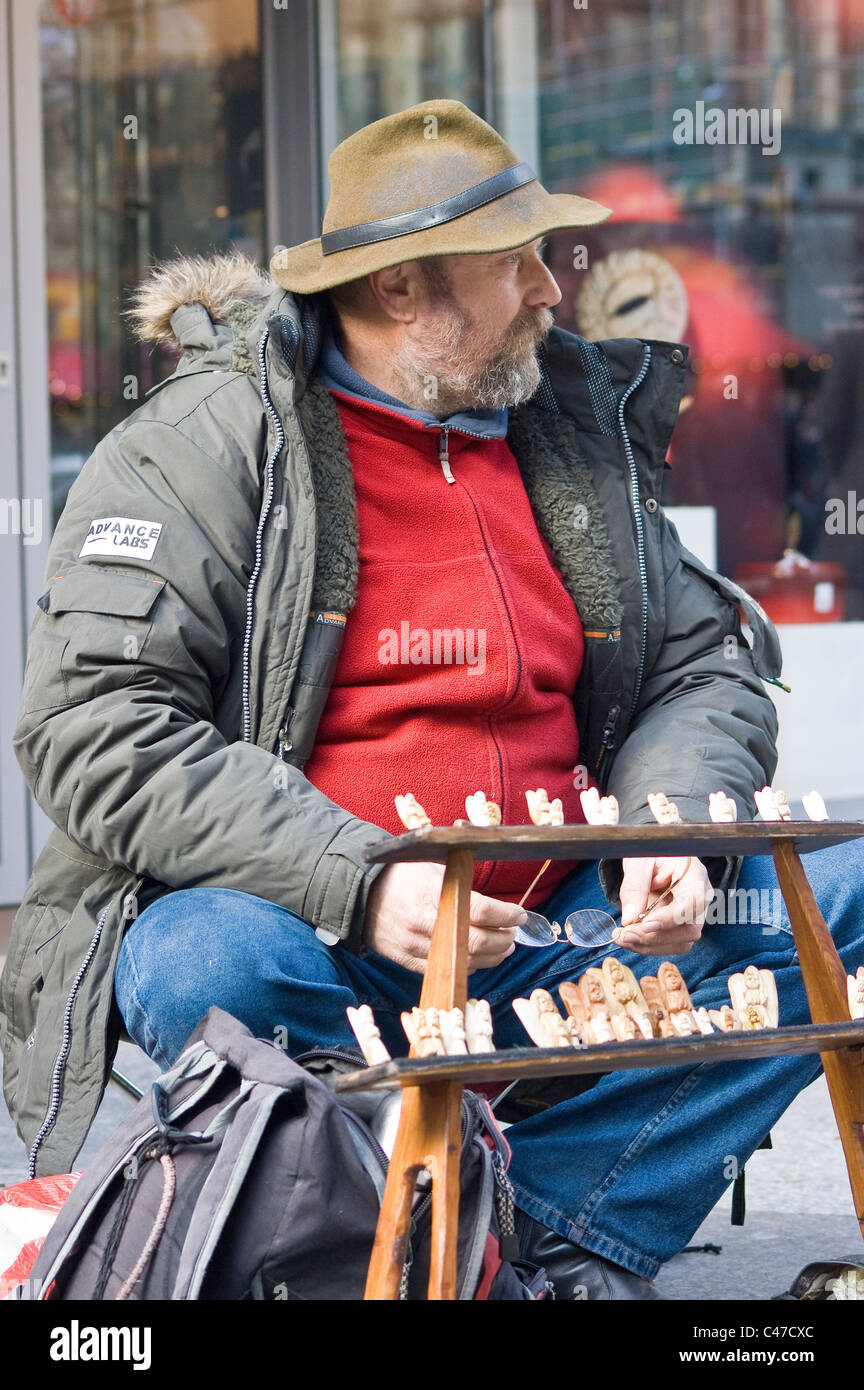 Homme assis à l'extérieur dans une rue de la ville exploitant un petit écran d'échecs, portant un chapeau et un manteau d'hiver. Banque D'Images