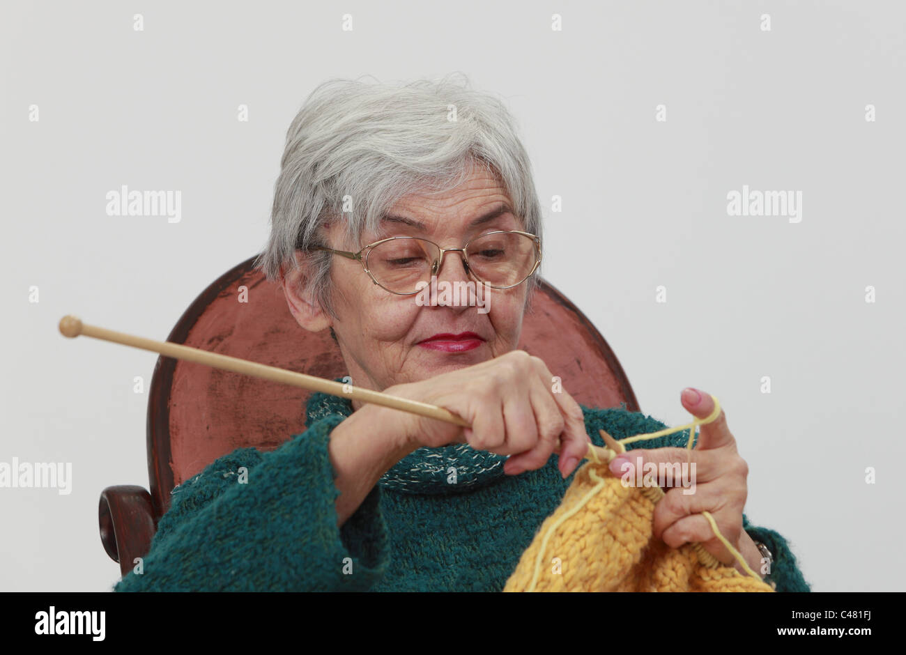 Portrait d'une vieille femme,tricot sur un arrière-plan gris. Banque D'Images