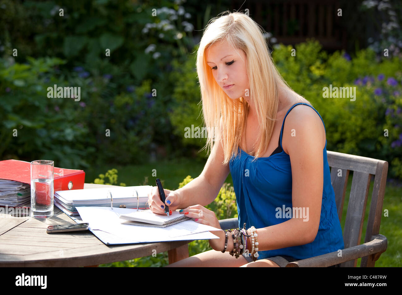 Jeune étudiante qui étudient à l'extérieur dans le jardin avec le bloc-notes et des fichiers pour les examens Banque D'Images