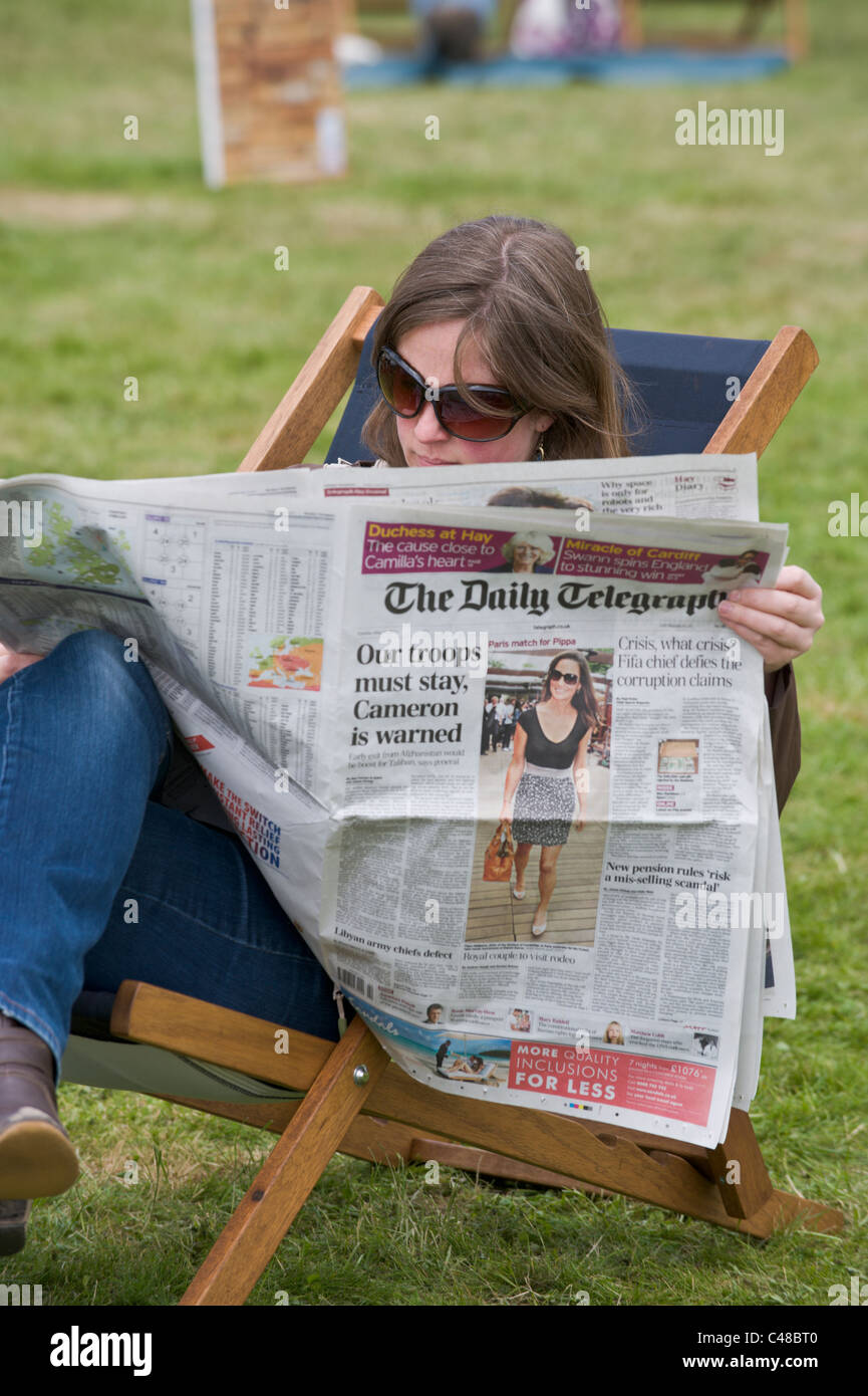 Jeune femme lisant le journal Daily Telegraph assis dans une chaise longue sur l'herbe au Hay Festival 2011 Banque D'Images