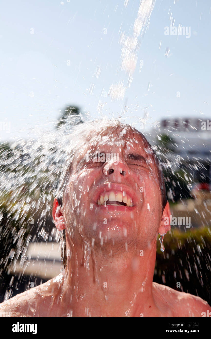 Parution du modèle homme sur des vacances lave ses cheveux sous la douche avec les projections d'eau. Banque D'Images